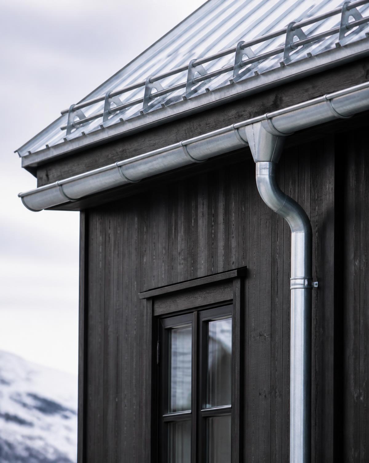 Takrenne, nedløp og snøfanger i metall på mørk trefasade